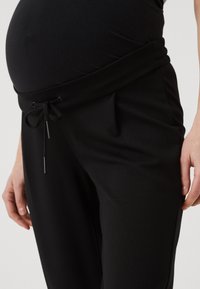 Sorte svangerskapsbukser i en myk, elastisk stoff. Har en bred, foldet midjebånd med justerbar snor for komfort.