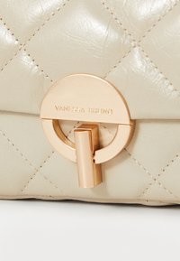 Jasnobeżowa torebka skórzana, pikowana, z okrągłym zapięciem w złotym kolorze z nazwą "Vanessa Bruno". Gładka faktura i elegancki design.