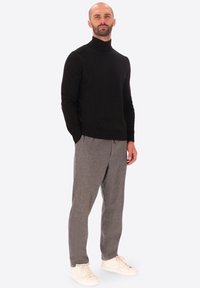 Maglione nero a collo alto abbinato a pantaloni grigi chiari e sneakers bianche. L'outfit presenta un design semplice e pulito con un tessuto testurizzato.