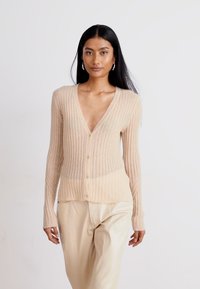 Cardigan a coste beige realizzato in tessuto leggero, con scollatura a V profonda, chiusura a bottoni e maniche lunghe. Texture liscia, senza motivi.
