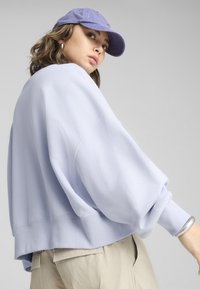 Sweat à manches tombantes de couleur lavande clair oversize avec des poignets côtelés, associé à une casquette violette assortie. Texture de tissu douce.