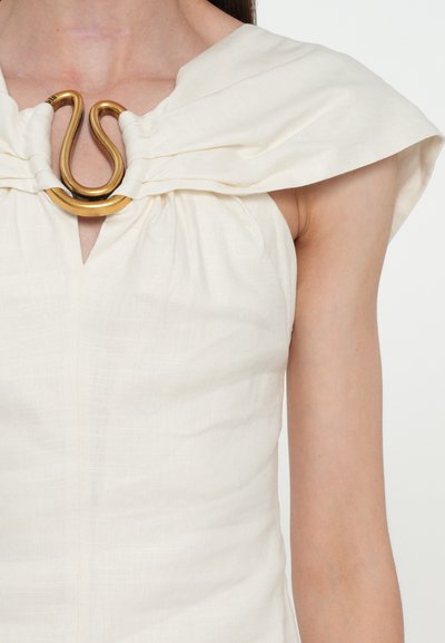 Cream-colored dress with a gathered neckline and a distinctive gold-tone hardware accent shaped like a snake. Smooth, textured fabric.