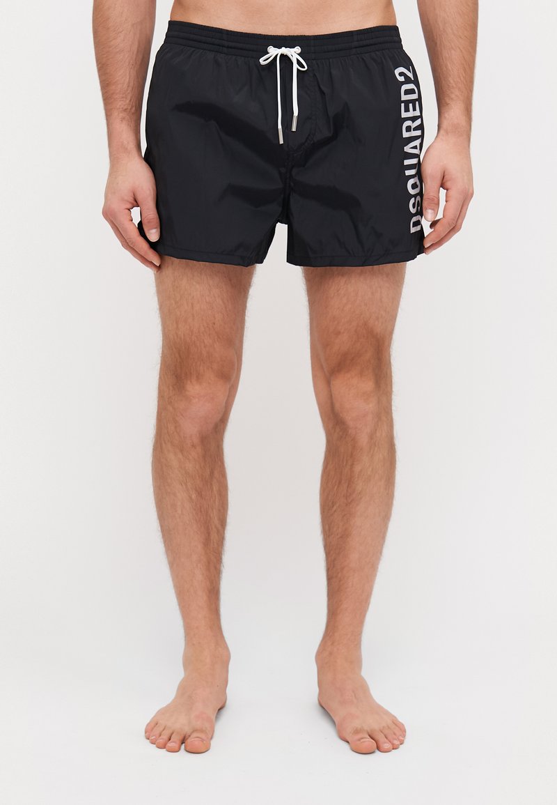 Shorts de bain noirs en matériau léger, dotés d'une taille avec cordon de serrage et d'un grand texte logo blanc sur le côté. Texture lisse.