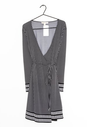 Czarna i biała sukienka w kropki z głębokim dekoltem w serek, długimi rękawami, wiązaniem w talii oraz mankietami i dołem w wzór houndstooth.