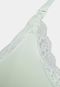Sutiã verde-claro com renda na borda superior. O tecido liso, as alças ajustáveis e os delicados detalhes em renda floral realçam o design.