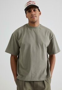 Tricou din bumbac de culoare verde măslin, cu mâneci scurte și guler rotund, având o textură netedă și un croi lejer.
