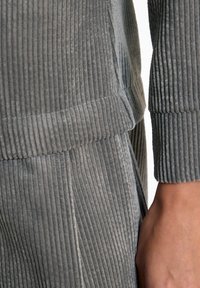 Graue Kordstoff-Loungewear mit vertikal gerippter Textur. Nahaufnahme des Bündchens und Abschlussteils mit glattem Finish und lässiger Passform.