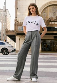 Witte t-shirt met "PARIS" in zwarte letters. Grijs gestreepte wijde broek en witte sneakers complementeren de outfit.
