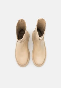 Stivaletti alla caviglia in pelle beige con finitura liscia, punte arrotondate e cuciture decorative intorno alla suola. Dotati di linguetta per facilitare la calzata e suola in gomma lavorata.