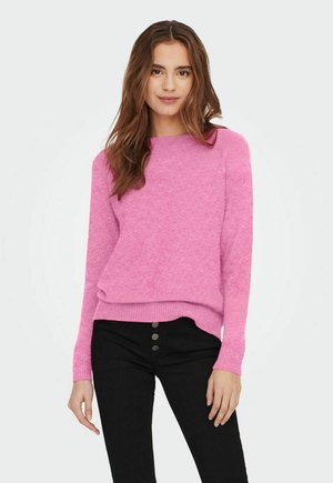 Pull en rose vif avec un col rond, des manches longues et un ourlet côtelé. Associé à un pantalon noir avec des accents de boutons. Texture douce.