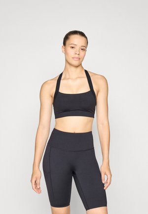 Svart atletisk crop topp med firkantet hals og brede stropper, kombinert med høy midje svarte sykkelshorts med sidelommer.