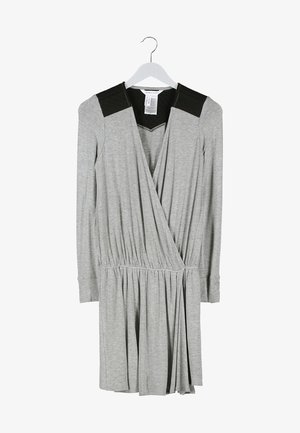Robe enveloppante grise à manches longues avec des accents noirs aux épaules, taille élastique et jupe évasée. Portée avec une pochette noire et des collants opaques.
