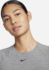 Rostro de una persona con piel suave, ojos oscuros y cabello peinado hacia atrás, vistiendo una camiseta deportiva Nike de color gris claro.