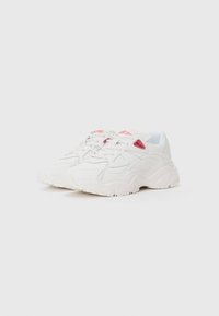 Chunky white sneakers with textured leather, rounded toe, thick rubber sole, and red accents on sides and tongue. Laced design.