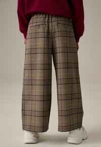Pantaloni a gamba larga a scacchi in tonalità beige, blu navy e verde, caratterizzati da una consistenza morbida, vita elastica e due tasche posteriori.