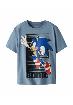 Vaaleansininen puuvillapaita, jossa on grafiikka juoksevasta sinisestä siilistä, punaisista kengistä ja mustista yksityiskohdista sekä "SONIC"-teksti alaosassa.