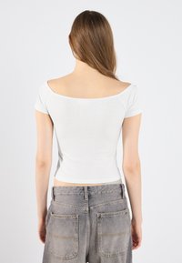 Baltā ribota īsām piedurknēm top ar off-the-shoulder dekoltē, apvienots ar augstās jostasvietas pelēkām džinsām, kam ir izteikti aizmugurējie kabatas.