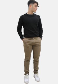 Zwarte ronde hals trui, beige chino's en witte sneakers. Slank pasvorm ontwerp, soepele textuur en contrasterende kleuren.