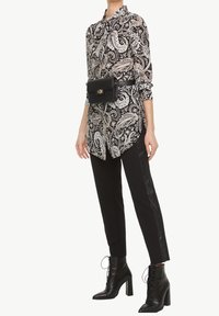 Black and white paisley print shirt with long sleeves, worn with black trousers featuring a shiny side stripe; paired with black ankle boots and a belt bag.
