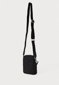 Μαύρη υφασμάτινη τσάντα crossbody με ορθογώνιο σχήμα, ρυθμιζόμενο λουρί και ασημένιες λεπτομέρειες. Λείος υφή, μινιμαλιστικός σχεδιασμός.