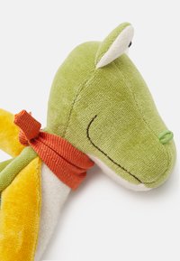 Green plush dragon toy with textured fabric, orange fabric ribbon, embroidered face details, and yellow accents on wings.