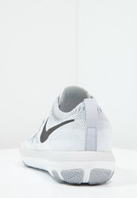Buty sportowe Nike, głównie z białej siateczki, czarne logo Swoosh, teksturowana podeszwa z szarymi akcentami, niskoprofilowy design z tylna pętlą do zakładania.