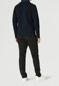 Suéter de punto azul marino con cuello alto; corte ajustado. Combinado con pantalones negros y zapatillas blancas; diseño sencillo sin patrones ni adornos.
