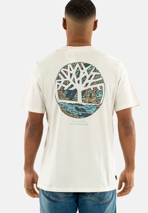 T-shirt en coton de couleur crème avec un graphique d'arbre circulaire au dos dans des teintes de bleu, marron et orange. Manches courtes et coupe décontractée.