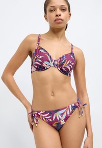 Ensemble soutien-gorge et bikini violet avec un motif de feuilles tropicales. Comprend des bretelles réglables, un nœud décoratif au niveau de la poitrine et un bas de bikini à nouer sur les côtés.