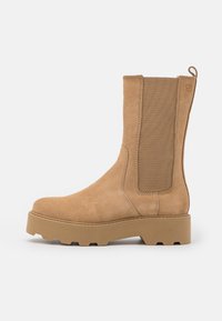 Tan suede ankle boot with elastic side panels and a raised rubber sole. Features a loop at the back for easy wear.