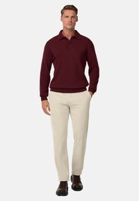 Burgunderfarbener Pullover mit Kragen und drei Knöpfen, kombiniert mit hellbeigen Hosen und dunkelbraunen Schnürstiefeln.