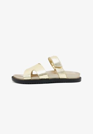Flat sandal with gold metallic straps, a black sole, and an adjustable ankle strap with a buckle closure.