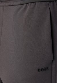 Grå sweatpants fremstillet af blødt, struktureret stof med snoretræk i taljen og et præget "BOSS" logo på venstre side.