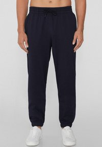 Pantalones jogger azul marino con cinturilla el�ástica, cordón y tobillos ajustados, hechos de una tela suave, combinados con zapatillas blancas.
