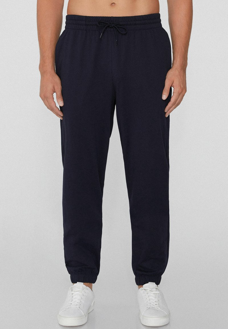 Pantalones jogger azul marino con cinturilla elástica, cordón y tobillos ajustados, hechos de una tela suave, combinados con zapatillas blancas.