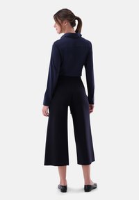 Navy long-sleeve shirt with a collar, paired with navy wide-leg trousers. Smooth, lightweight fabric; features clean lines and tailored fit.