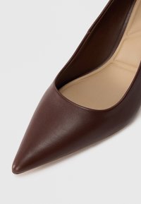 Bottines à talons pointus en cuir marron avec une texture lisse et un intérieur nude, mettant en avant une silhouette élégante et un design décolleté.