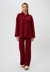 Set di abbigliamento da casa color bordeaux, composto da una camicia oversize con colletto e bottoni e pantaloni a gamba larga, realizzato in un morbido tessuto testurizzato.