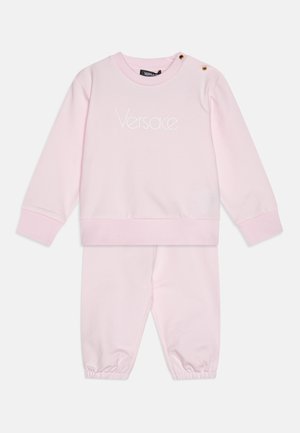 Ensemble de survêtement en coton rose comprenant un sweat-shirt à col rond avec logo brodé et accents à boutons-pression. Pantalon avec poignets élastiques. Texture douce.
