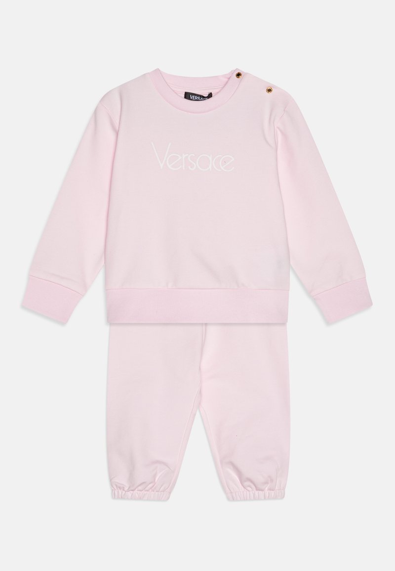 Roza bombažna trenirka z majico s poudarjenim ovratnikom, ki ima vezeno logo in gumbi s pritiskom. Hlače z elastičnimi manšetami. Mehka tekstura.