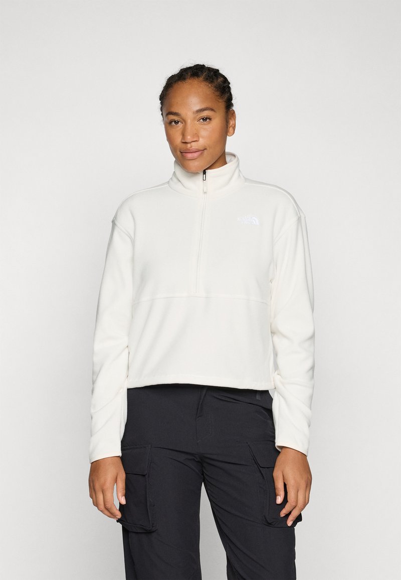 Pullover in felpa color crema chiaro con colletto a mezza zip, caratterizzato da un logo bianco sul lato sinistro del petto e maniche lunghe. Abbinato a pantaloni scuri.