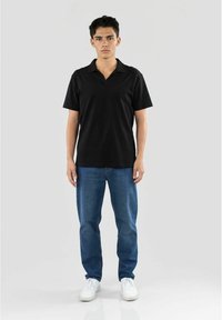 Sort polo t-shirt med V-hals, parret med blå jeans og hvide sneakers. Modellen står oprejst foran en neutral baggrund.