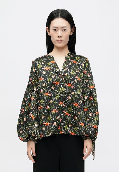 Blouse noire à motifs floraux avec des manches bouffantes, présentant des motifs de fleurs rouges et blanches, un décolleté en V et un design à boutons sur le devant. Texture de tissu douce.