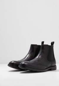 Zwarte leren Chelsea boots met geperforeerde accenten, elastische zijpanelen en een lage hak. Glad textuur met een afgeronde teenvorm.
