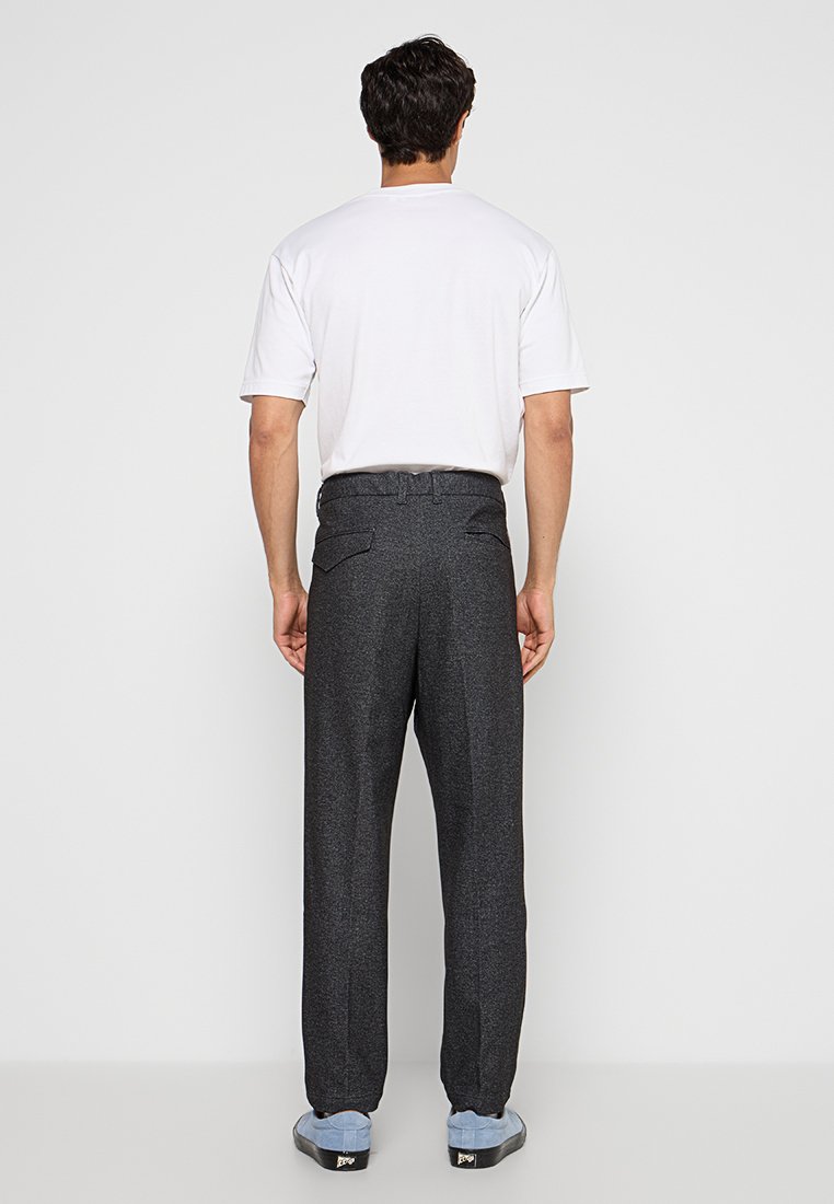 Graue, strukturierte Hose mit lockerer Passform, Gesäßtaschen und einem Bund. Kombiniert mit einem schlichten weißen T-Shirt und blauen Turnschuhen.