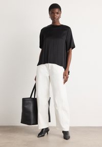 Svart satin topp med korte ermer og avslappet passform, kombinert med høyt liv hvite bukser og en svart totebag. Teksturert svarte hæler.