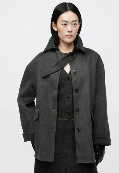 Tamsiai pilkas vilnonių paltas su juodu odiniu apykakle, dvigubais sagomis, šoninėmis kišenėmis ir laisvu siluetu. tekstūruota medžiaga ir sluoksniuotas dizainas.