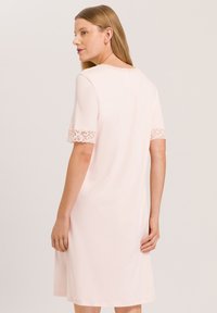 Vestido rosa claro con mangas cortas que presenta un acabado de encaje en los puños y el escote. Textura suave, forma en A y diseño a la altura de la rodilla.