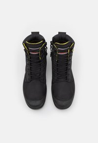 Botas negras impermeables de caña alta con ribetes amarillos, cuellos acolchados y cordones negros, mostradas desde arriba sobre un fondo blanco.