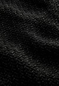Gros plan d'un tissu tricoté noir montrant une texture bouclée et des détails fins de fil avec des reflets lumineux subtils.